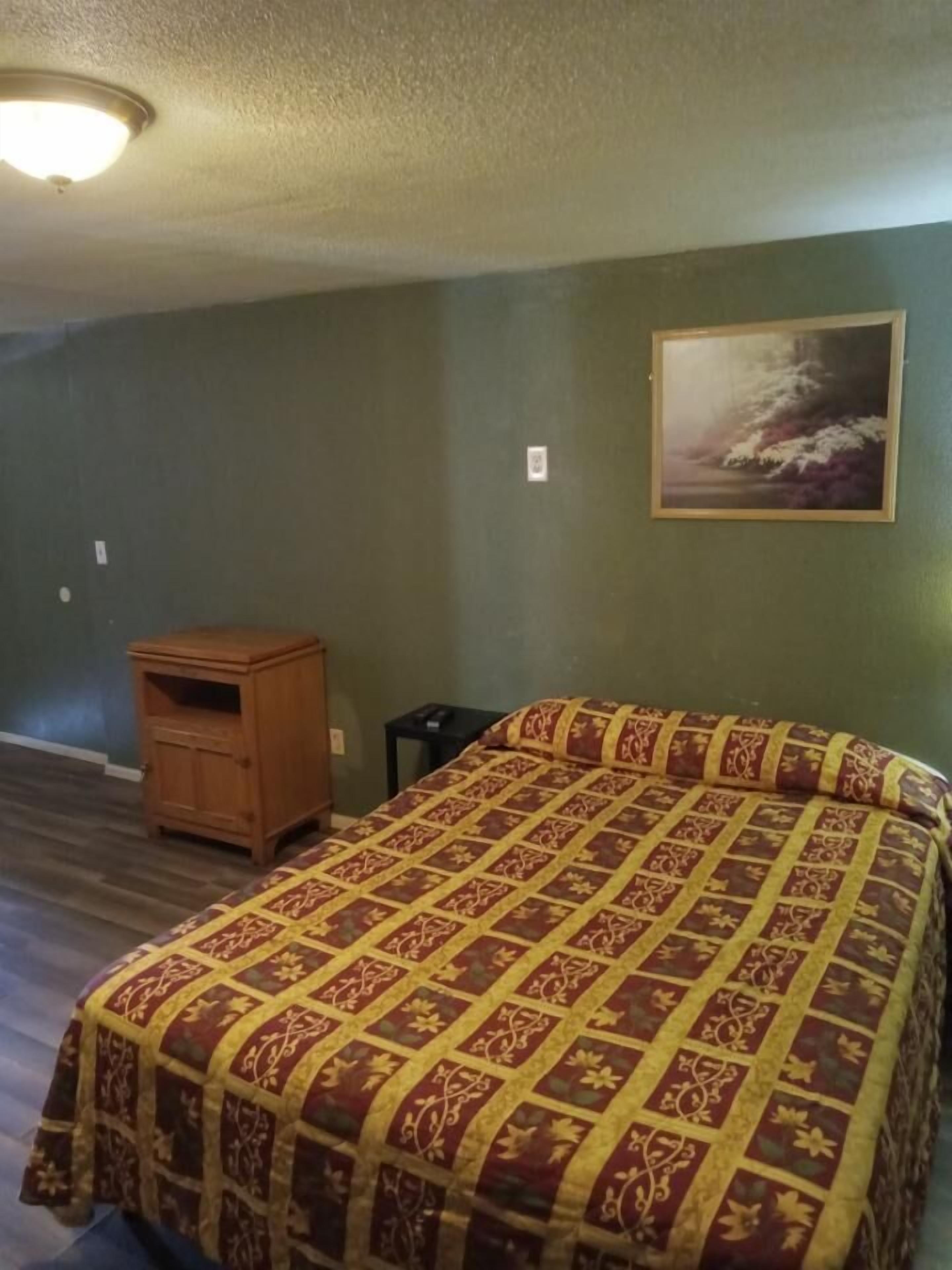Ein Zimmer mit einem großen Bett, einem hölzernen Nachttisch, einem kleinen Tisch und einem Bild an der Wand.