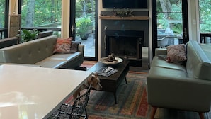 A modern living room with a fireplace, large windows, and a flat-screen TV. - Private Wooded Acre, Soaring Windows in Nat’l Park, 2 blocks to the beach (Gary)