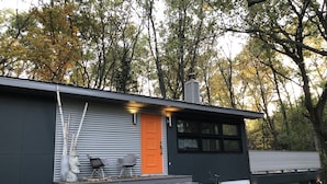 A modern house with a gray exterior, a bright orange door, and a small porch with two chairs and two pumpkins. - Private Wooded Acre, Soaring Windows in Nat  ’l Park, 2 blocks to the beach (Gary)