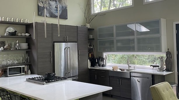 A modern kitchen with a central island, bar stools, and a view of trees through large windows. - Private Wooded Acre, Soaring Windows in Nat’l Park, 2 blocks to the beach (Gary)