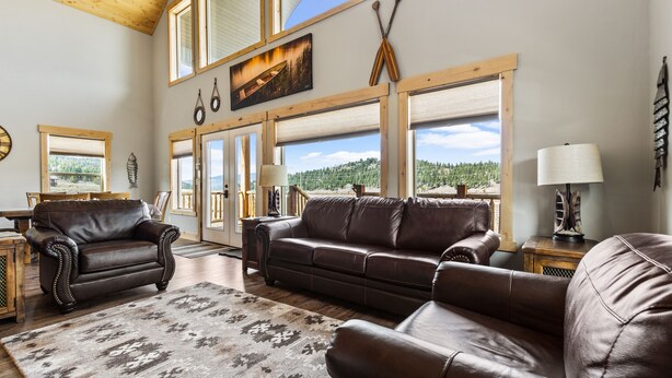 A spacious living room with leather sofas, a wooden coffee table, and a large window offering a scenic view. - The Yellowstone Hideaway - Beautiful 3 Bedroom, 2 Bath Cabin- Sleeps 10 (Island Park)