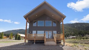 A two-story lodge with a wooden deck, large windows, and a mountain backdrop. - The Yellowstone Hideaway - Beautiful 3 Bedroom, 2 Bath Cabin- Sleeps 10 (Island Park)