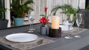 A table set with a white plate, two wine glasses, a candle, and a small vase with a red flower.