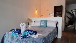 A hotel room with a bed, a nightstand, a lamp, a wall-mounted TV, and a staircase in the background.