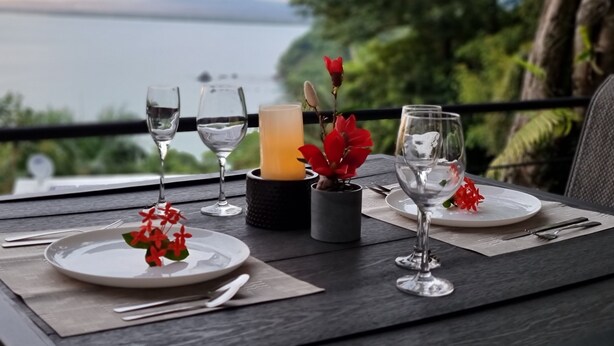 A table set for two with wine glasses, a candle, and a flower centerpiece, overlooking a scenic view.