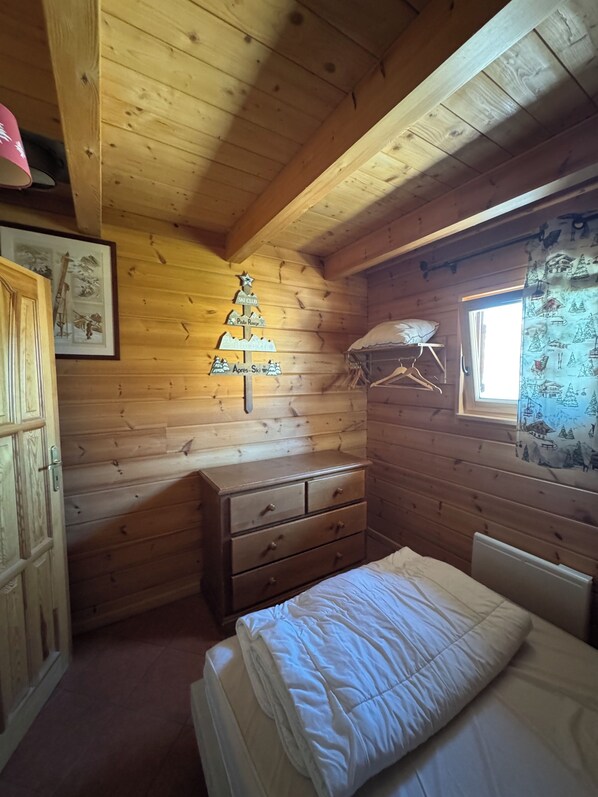 A wooden cabin room with a bed, a dresser, a window with a curtain, and a wall-mounted sign.