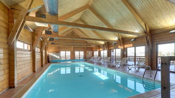 Une cabane en bois avec une piscine, des chaises longues et de grandes fenêtres.