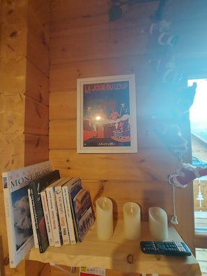 A wooden interior with a shelf holding books, candles, and a remote control.