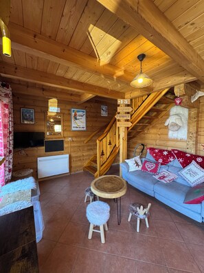 A wooden interior with a staircase, a blue sofa with decorative pillows, and a small round table. - La Joue du Loup Log Cabin - Sleeps 11 (agnières en Dévoluy)