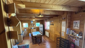 A wooden cabin interior with a dining area, kitchen, and seating space. - Log cabin La Joue du Loup - sleeps 11 (agnières en Dévoluy)