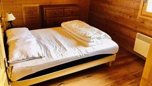 A wooden cabin bedroom with a bed, a nightstand, a dresser, and a window. - Log cabin La Joue du Loup - sleeps 11 (agnières en Dévoluy)