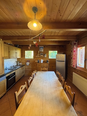 A wooden cabin kitchen with a central dining table, wooden cabinets, a stove, and a refrigerator.