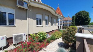 A building with air conditioning units, a curved roof, and a garden with flowers and shrubs. - Holiday apartment newly renovated with air conditioning (Siófok)