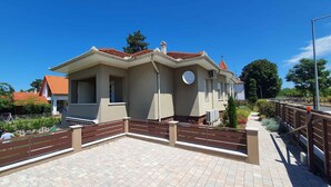 A two-story building with a tiled roof, a clock on the facade, and a paved courtyard with a wooden fence. - Holiday apartment newly renovated with air conditioning (Siófok)