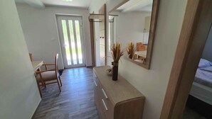A hallway with a wooden chair, a desk with a vase, and a mirror reflecting a dining area. - Holiday apartment newly renovated with air conditioning (Siófok)