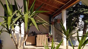 A covered outdoor area with plants, a wicker sofa, and a table with items on it. - Studio with air conditioning and WLAN (Pula)