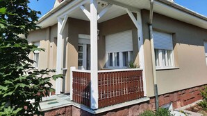 A two-story house with a red-tiled roof, a porch with white railings, and a brown fence.