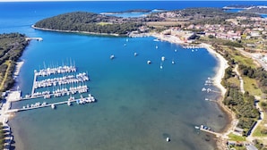 Vista aèria d'una marina amb vaixells amarrats, envoltada per una localitat costanera amb edificis i vegetació.