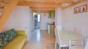 Un interior modern amb un sostre de fusta, una zona de menjador amb taula de vidre i una cuina amb armaris verds.