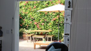 An outdoor patio with a wooden table and chairs, a hanging umbrella, and a potted plant.