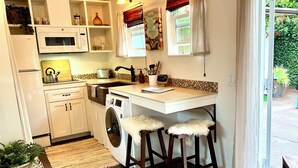 A compact kitchen with a washing machine, a dining area with stools, and a view of the outside.