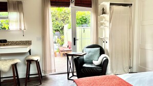 A room with a bed, a chair, a table, and a view of the outside.