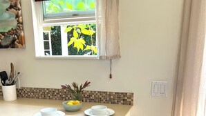 A kitchen with a white countertop, two stools with fluffy seats, a window with a view of greenery, and a tiled backsplash.