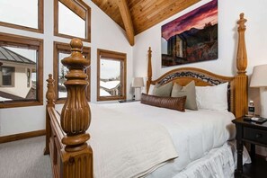Una camera da letto con un letto in legno, ampie finestre, un quadro appeso e vista su un edificio.