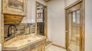 Un baño con lavamanos de piedra, armarios de madera y una puerta con ventanal.