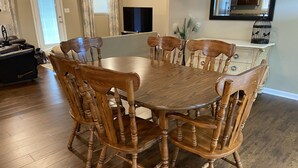 Un coin repas avec une table et des chaises en bois, un téléviseur et une cuisine en arrière-plan.