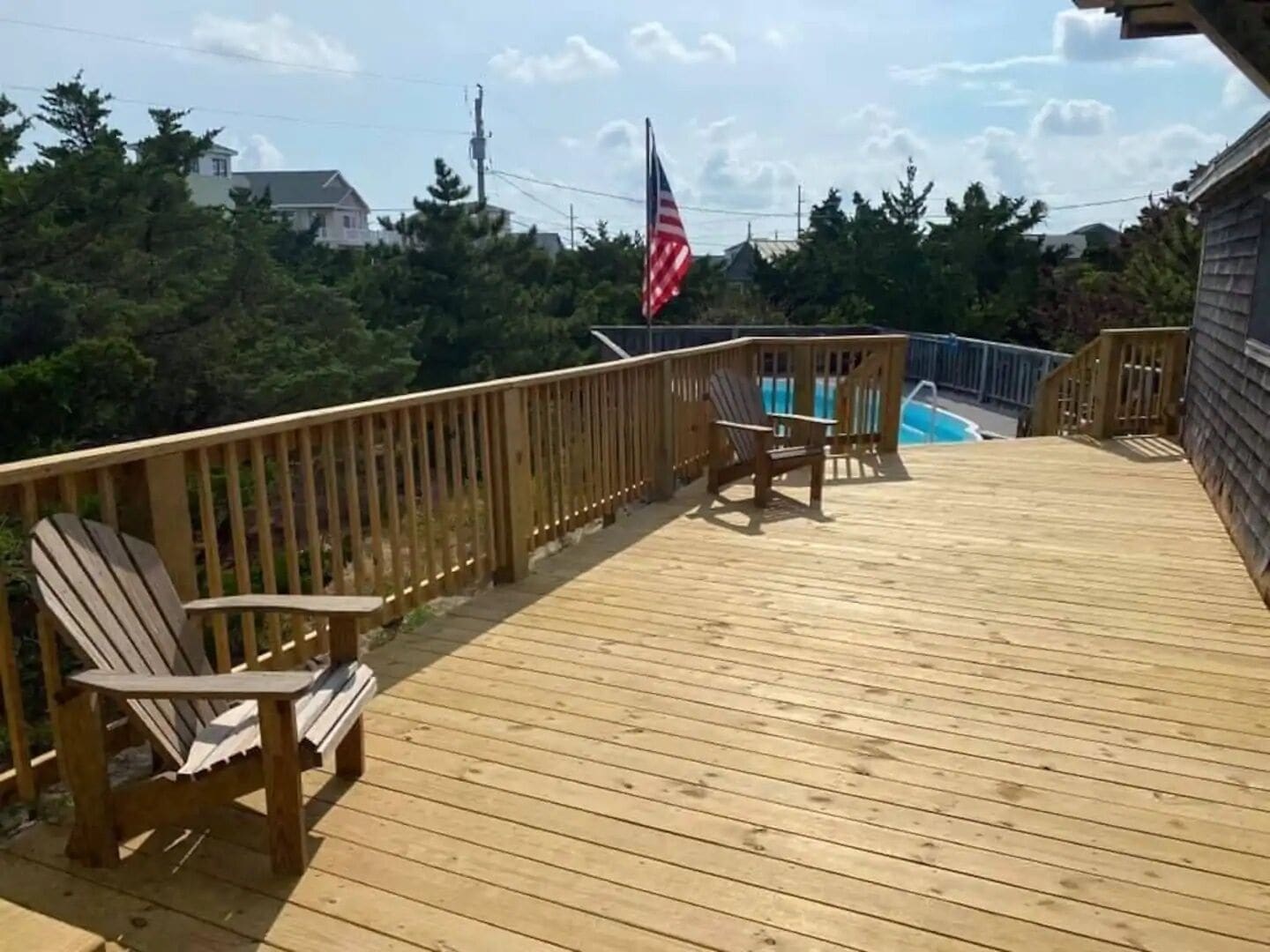 A wooden deck with a flag, a pool, and a chair.
