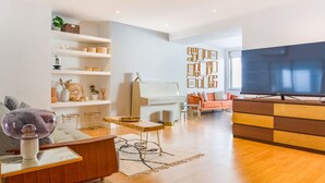 A modern living room with a wooden floor, a flat-screen TV, a sofa, a coffee table, and a bookshelf.