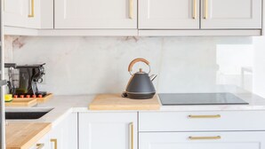 A modern kitchen with white cabinets, gold handles, a black kettle, and a coffee maker on the counter.