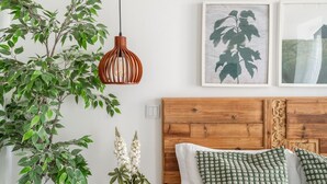 A bedroom with a wooden headboard, a hanging pendant light, a potted plant, and framed botanical prints on the wall. - Elegant Luxury Old Town Studio-apt by Lisbeyond (Lisboa)