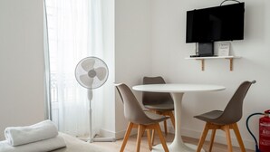 A modern room with a round table, four chairs, a standing fan, a flat-screen TV on a shelf, and a fire extinguisher. - Elegant Luxury Old Town Studio-apt by Lisbeyond (Lisboa)