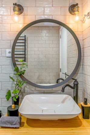 Bathroom features a large round mirror, a white vessel sink, and a potted plant.