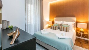 A modern hotel room with a large bed, bedside lamps, a small table with decorative items, and a view of the outdoors through sheer curtains. - Lively 2 Bedroom Apartment in Iconic Alfama by Lisbeyond (Lisboa)