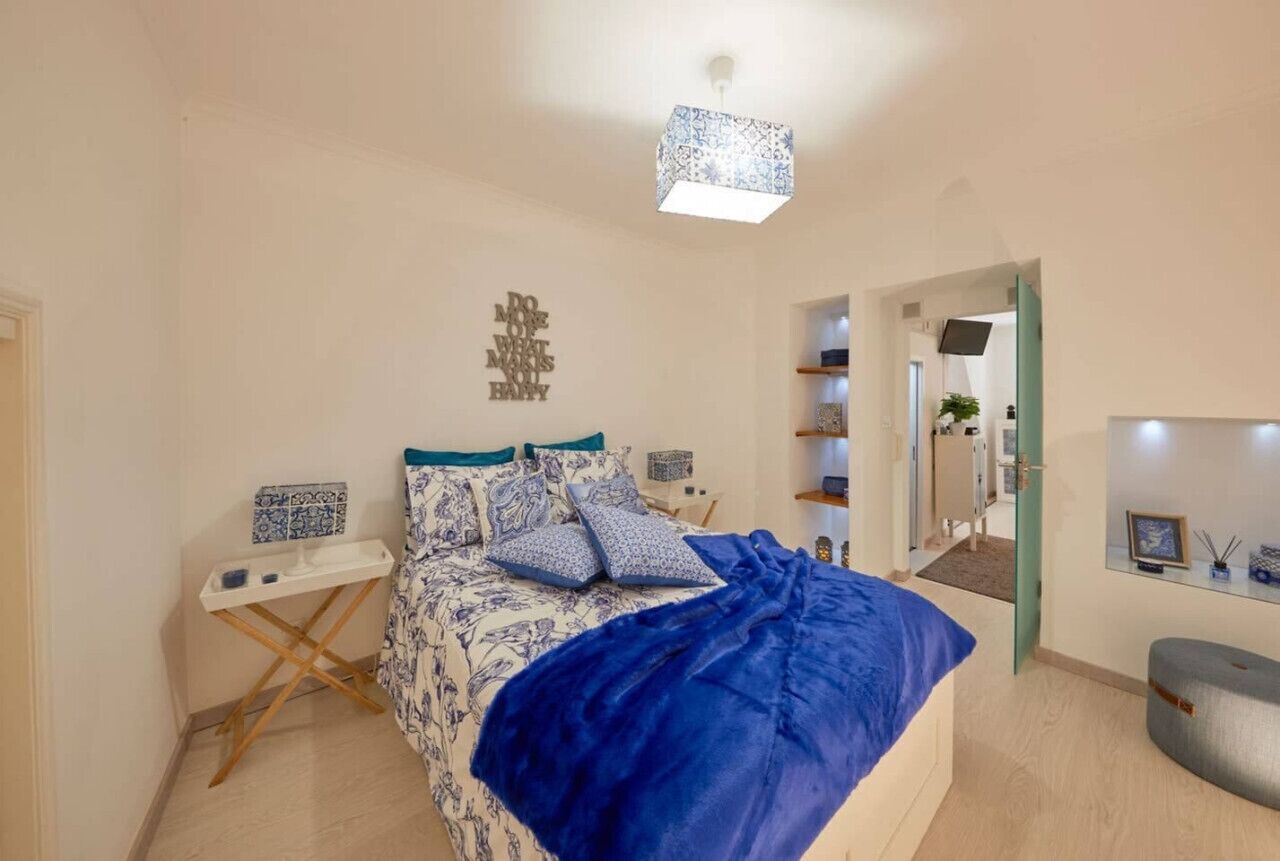 A bedroom with a bed, bedside tables, a mirror, and a door leading to another room.