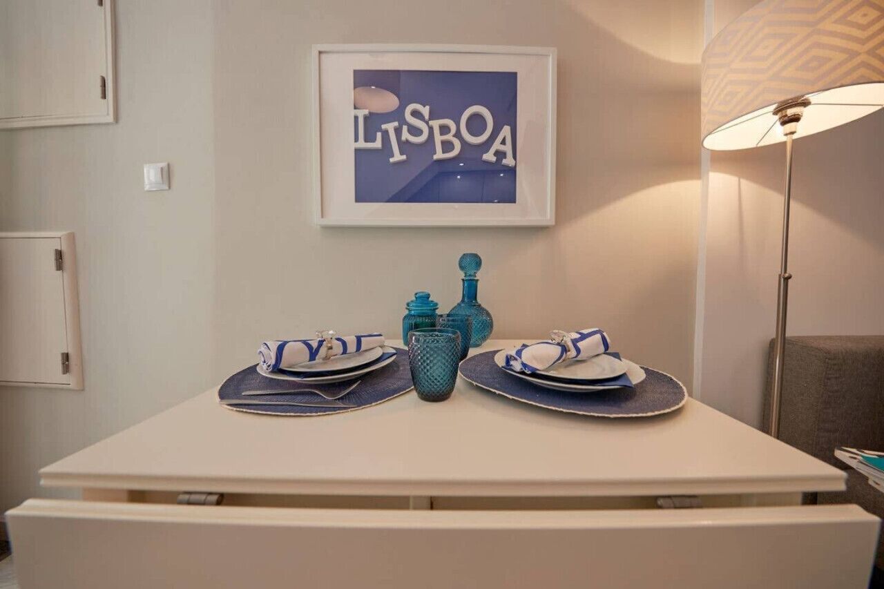Une table dressée avec des assiettes, des serviettes et de la verrerie bleue, et un panneau encadré portant l’inscription « LISBOA » accroché au mur derrière.