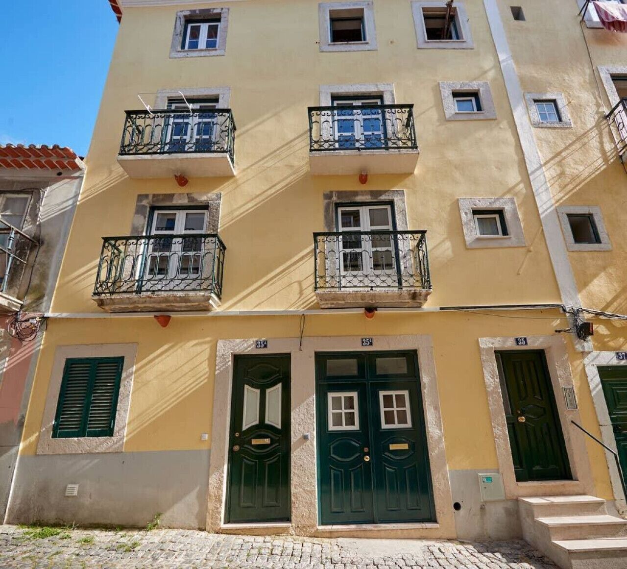 Un immeuble à plusieurs étages, doté de balcons, de portes vertes et d’un sol pavé.