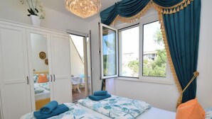 A bedroom with two beds, a window with curtains, a chandelier, and a view of the outside.