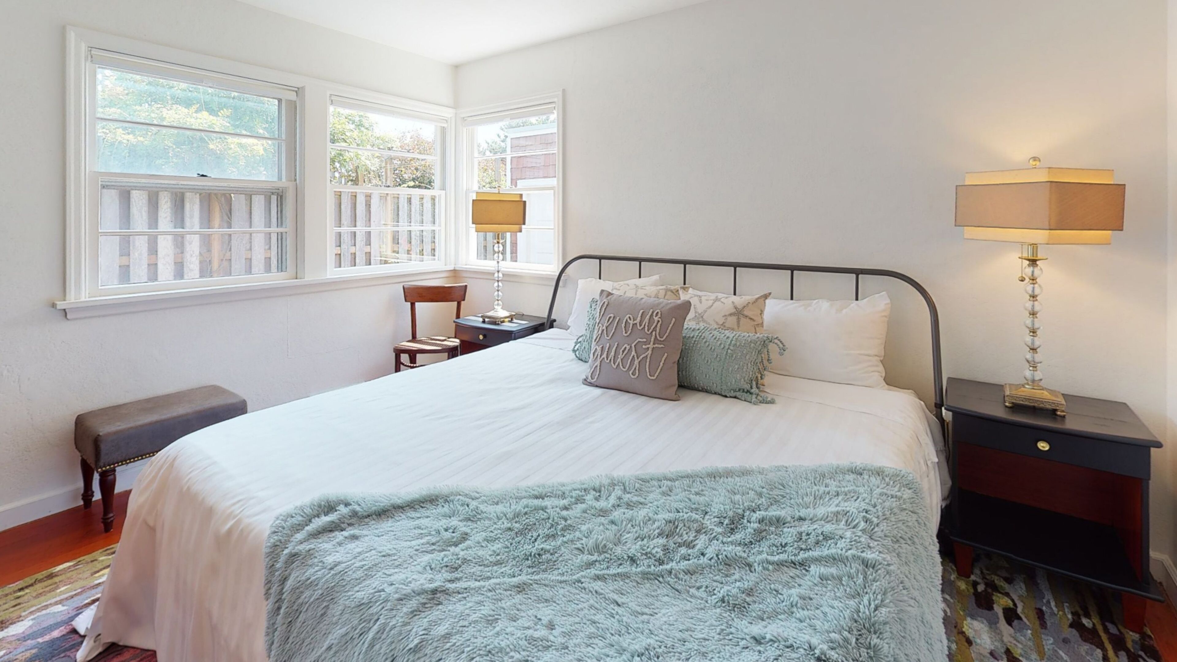A bedroom with a large bed, two bedside tables, a chair, and a window with a view of trees.