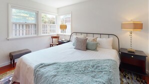 A bedroom with a large bed, two bedside tables, a chair, and a window with a view of trees.