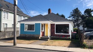 A small, single-story house with a dark roof, a yellow front door, and a blue siding.