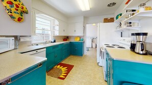 A compact kitchen with teal cabinets, white appliances, and a sunburst rug.