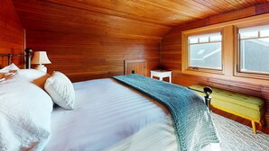 Een slaapkamer met houten lambrisering, een bed, een nachtkastje, een lamp en een raam.