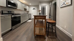 A modern kitchen with stainless steel appliances, a wooden table, and a bar stool. - Airy Modern 2BR/2BA - Parking + Laundry + Sleep 6 (San Jose)