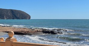 A coastal view with a rocky shoreline, a clear sky, and a distant cliff.