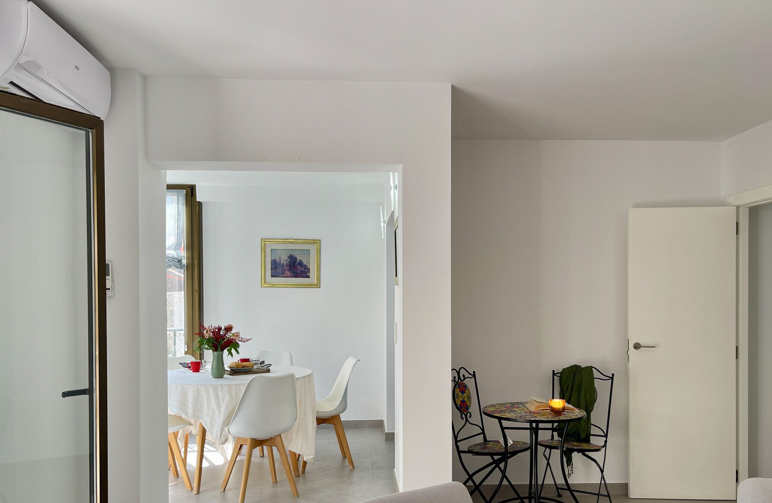A dining area with a table and chairs, a small table with a candle, and a door leading to another room.