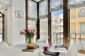 A dining area with a table set for two, a vase with flowers, and a window with curtains.